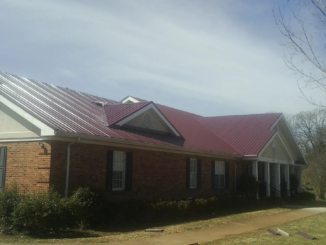Red metal roof with gabled entries on a long brick building, from a Hail Damage Roof Repair job in Woodville