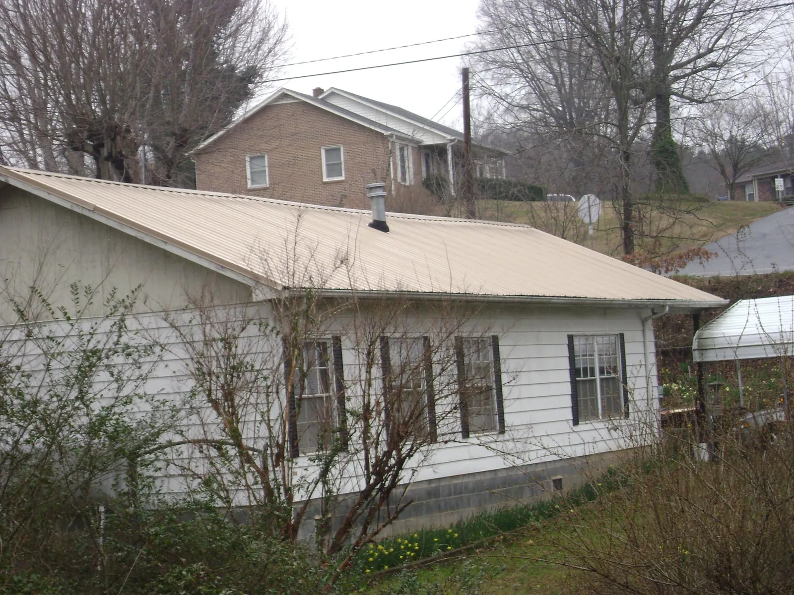 Tan metal roof on a white sided house set into a hillside — Commercial Roofing by Roofing Brothers in Woodville